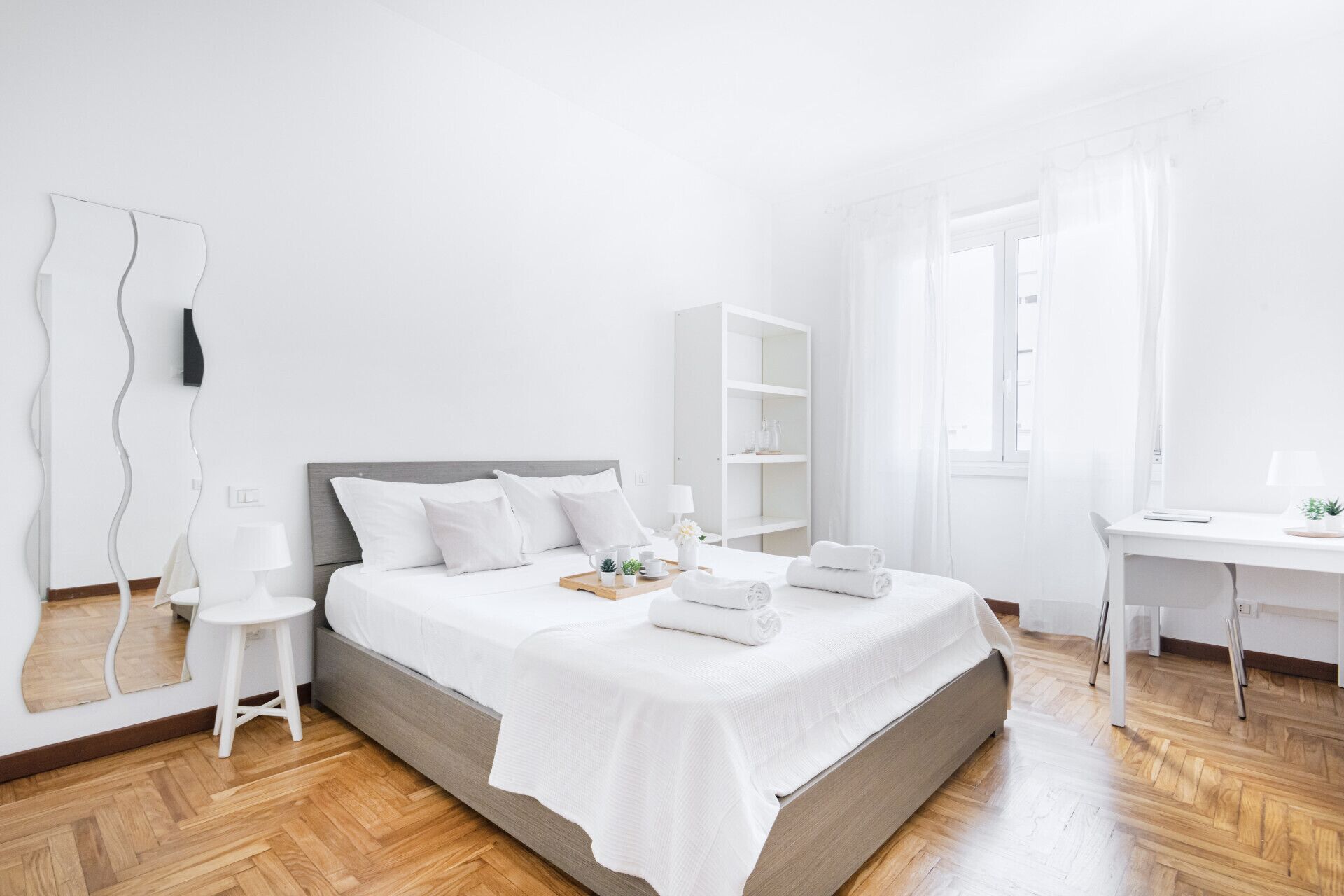 Moderni, pelkistetty hotellihuone, jossa on suuri sänky, työpöytä ja vaatekaappi.