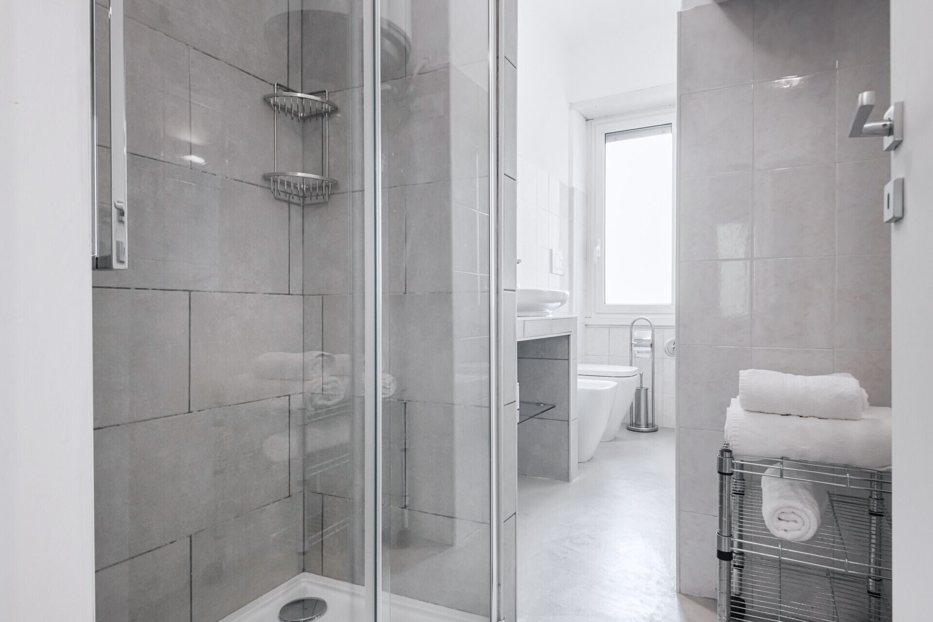 A modern bathroom with a glass-enclosed shower, a white sink, and a towel rack.