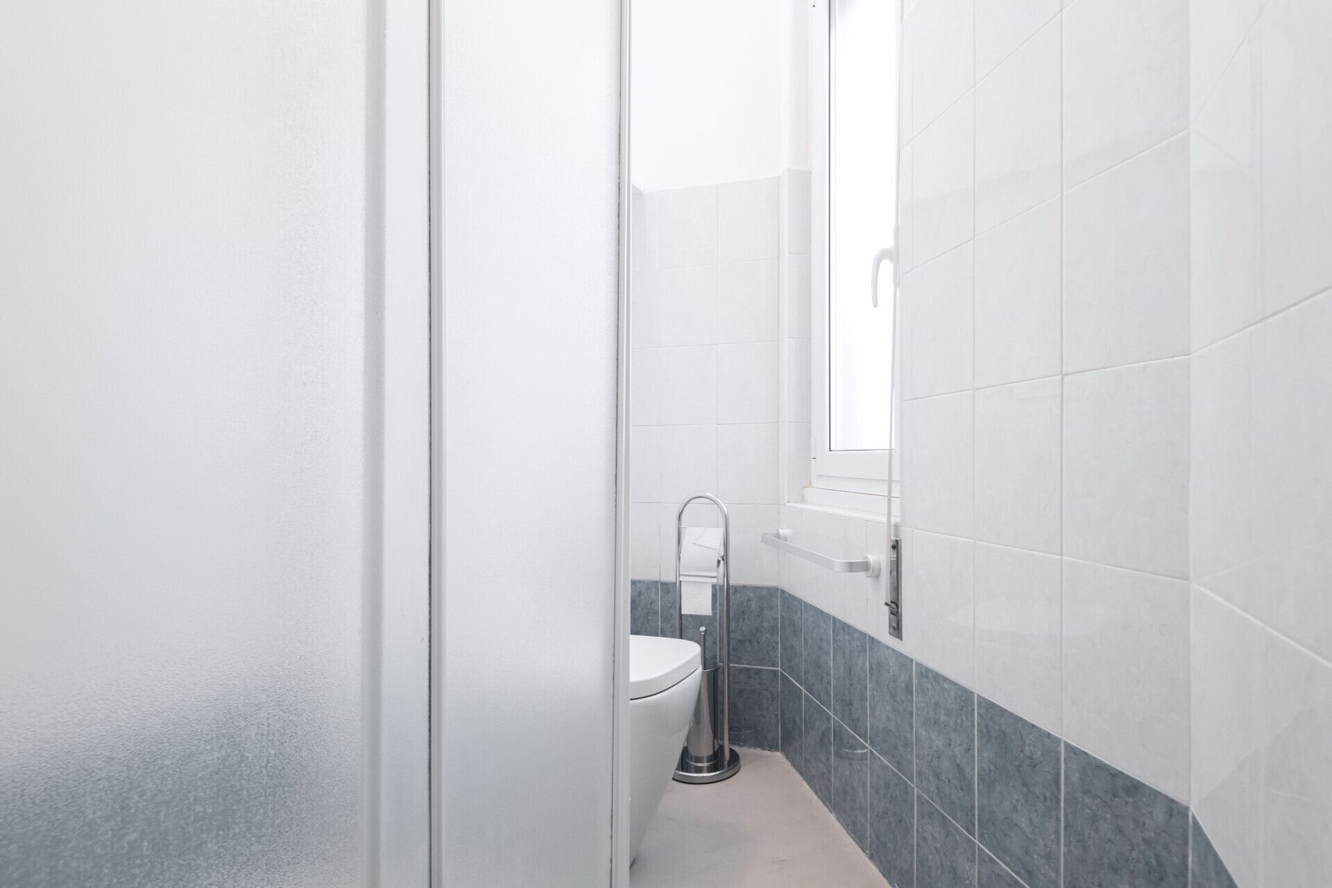 A bathroom with white and grey tiles, a white toilet, and a glass shower enclosure.