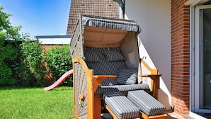 A sun lounger with a canopy, positioned on a brick patio adjacent to a building with a tiled roof.