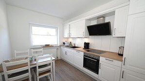A modern kitchen with white cabinetry, a wooden countertop, a built-in oven, a microwave, and a large flat-screen TV.