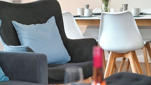 A modern living room with a dark grey sofa, a light blue pillow, and a white chair.