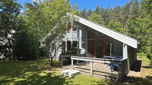 A modern wooden cabin with a deck, surrounded by lush greenery and trees. - Wildgans 83 - Classic Scandinavian vacation home for up to 6 people (Mirow)