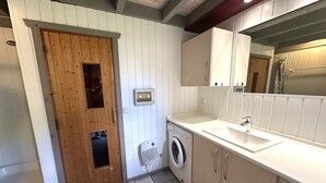 A compact laundry room with a washing machine, a dryer, a wooden door, and a white sink. - Wildgans 83 - Classic Scandinavian vacation home for up to 6 people (Mirow)