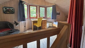 A cozy cabin room with a wooden interior, a desk with a chair, a bed, and a view of greenery through the windows. - Wildgans 83 - Classic Scandinavian vacation home for up to 6 people (Mirow)