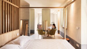 Une chambre d’hôtel avec un grand lit, deux fauteuils, un bureau et un miroir.
