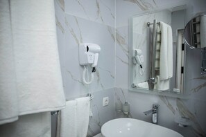 Une salle de bain avec un lavabo blanc, un miroir, un porte-serviettes et un sèche-cheveux fixé au mur.