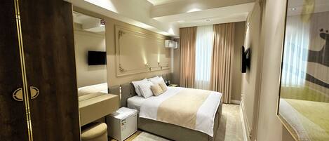 A modern hotel room with a large bed, a vanity with a mirror, a small seating area, and a large window with curtains.