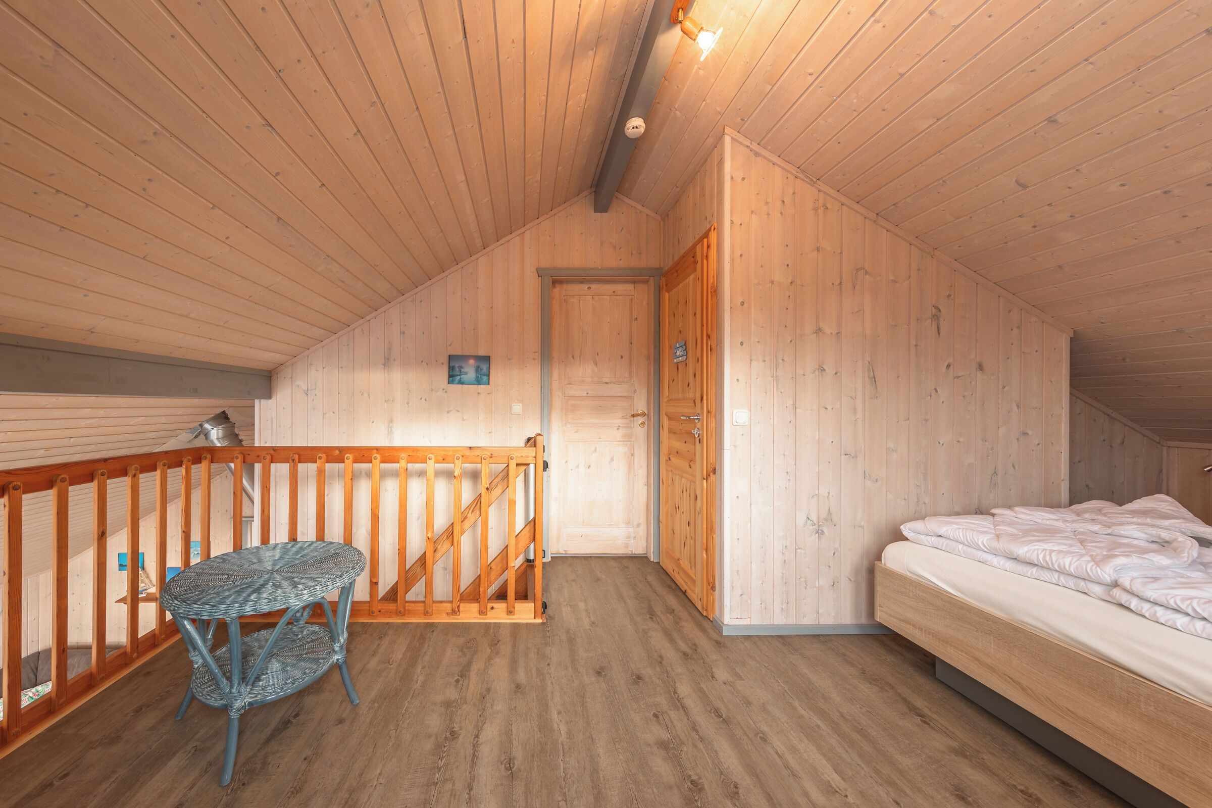 Ein Zimmer mit Holzwänden, einem Bett, einem kleinen Tisch und einer Treppe, die zu einer oberen Ebene führt.