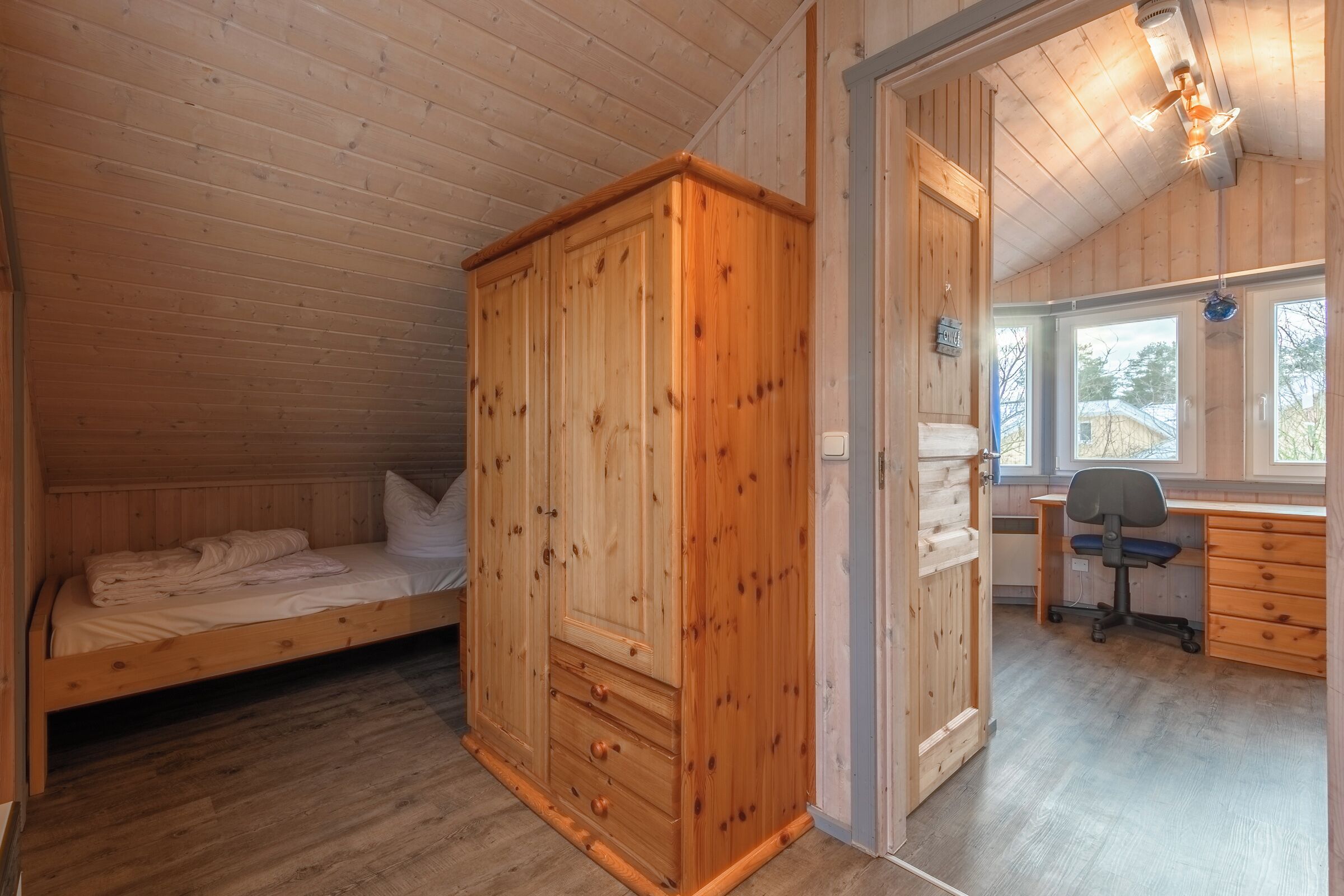 Ein Zimmer mit Holzwänden, einem Bett, einem Kleiderschrank und einem Schreibtisch mit Stuhl.