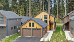 A row of modern wooden houses with grey exteriors and brown garages, surrounded by a forested area. - Harmony Haven - EV - Hot Tub - Pups Allowed (Cle Elum)