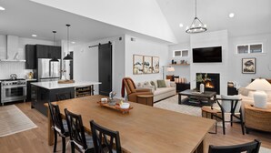 A modern kitchen with a dining area, a living room with a fireplace, and a TV mounted on the wall. - Harmony Haven - EV - Hot Tub - Pups Allowed (Cle Elum)