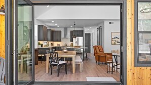 A modern kitchen with dark cabinetry, a wooden dining table, and a seating area with a leather chair. - Harmony Haven - EV - Hot Tub - Pups Allowed (Cle Elum)