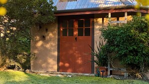 Una casa rústica con puerta roja, una ventana pequeña y techo de metal.