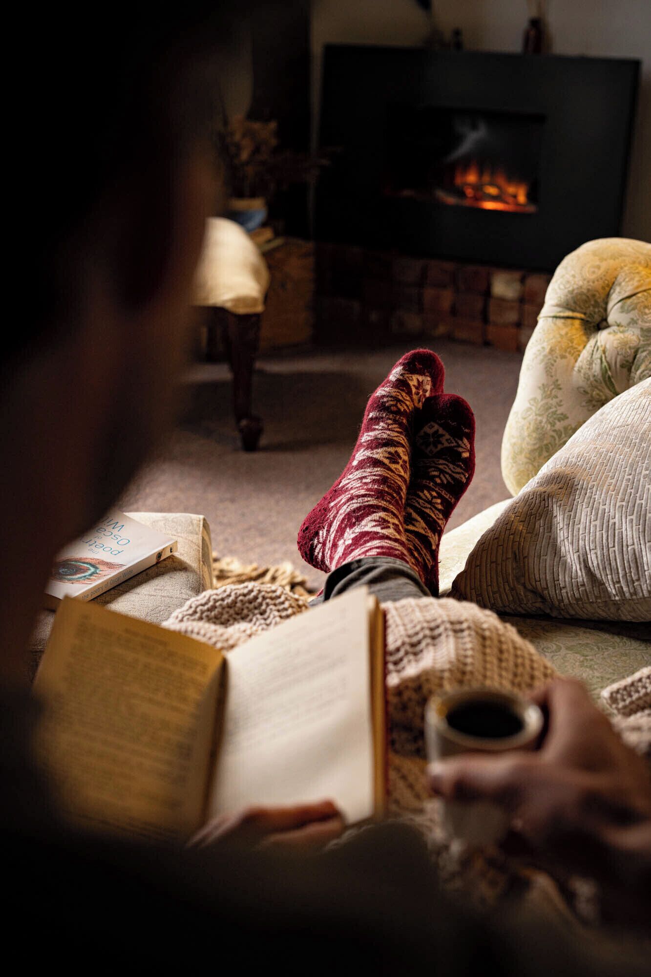Una persona leyendo un libro con una chimenea al fondo.