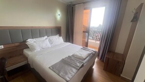 Ein Hotelzimmer mit einem großen Bett, einem Holzkopfteil, einem Nachttisch und Blick auf einen Balkon.