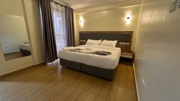 Una habitación de hotel moderna con una cama grande, suelo de madera, cabecero con iluminación integrada y un espejo en una pared.