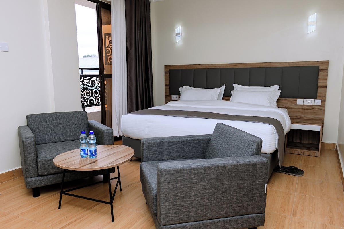 A hotel room with a bed, two armchairs, a small table with water bottles, and a view of the outdoors.