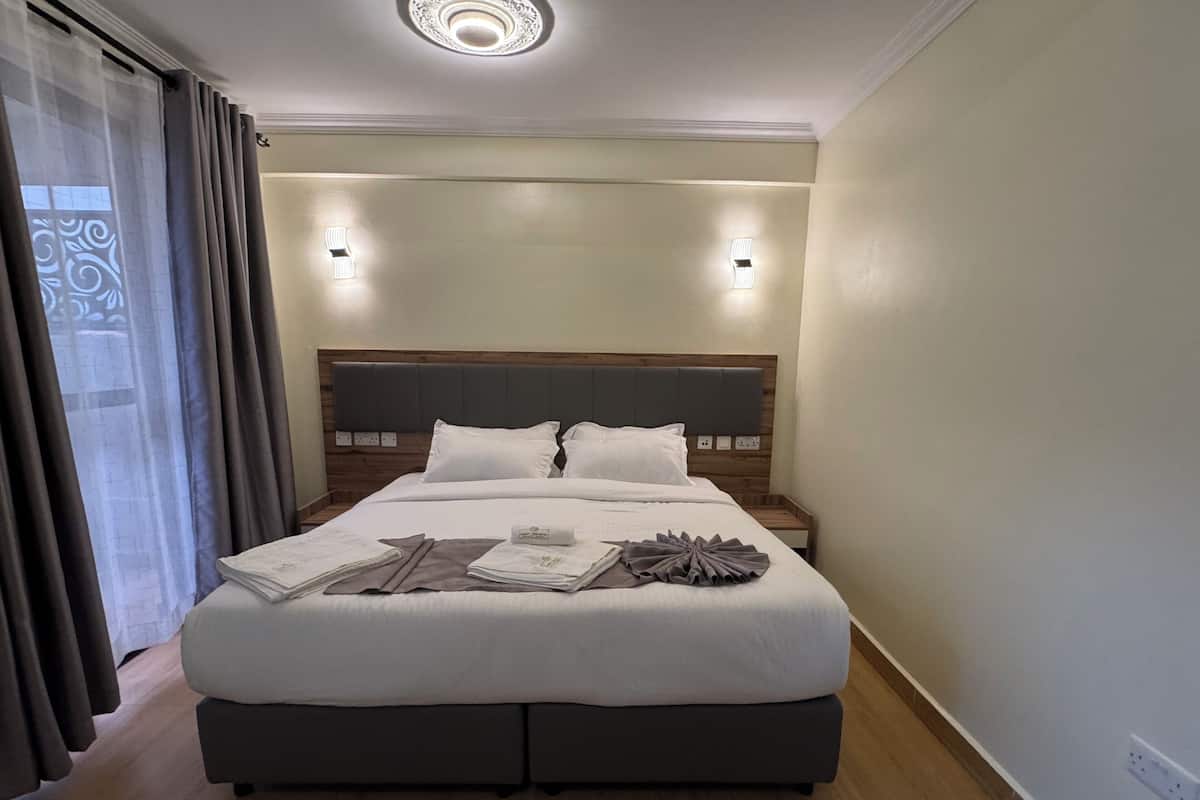 A neatly made bed with white linens and a decorative towel arrangement, a wooden headboard, and a modern light fixture above.