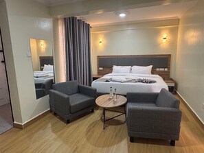 Habitación de hotel con una cama grande, dos sillones, una mesita redonda y un espejo en la pared.