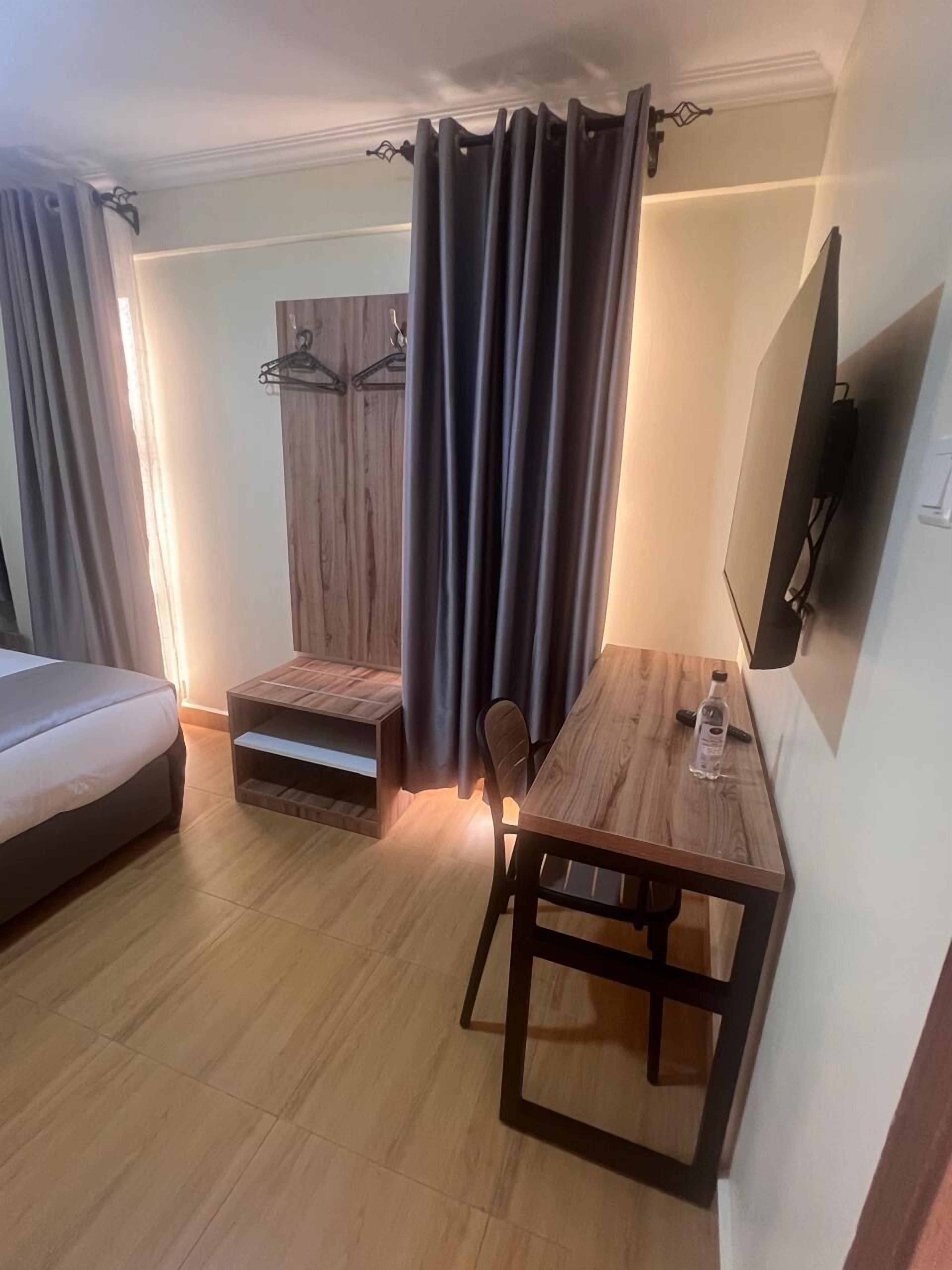 A compact hotel room with a bed, a small table with a chair, a TV mounted on the wall, and a wardrobe.