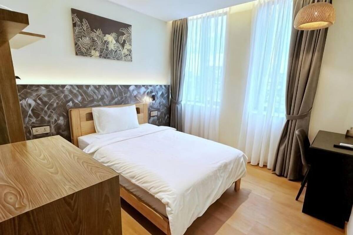 A hotel room with a bed, a desk, a chair, and a lamp.