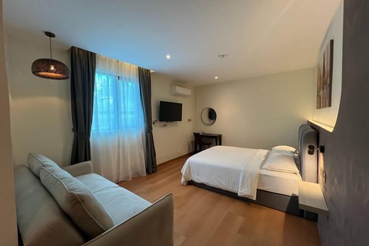 A modern hotel room with a sofa, a bed, a TV, and a wall-mounted air conditioner.