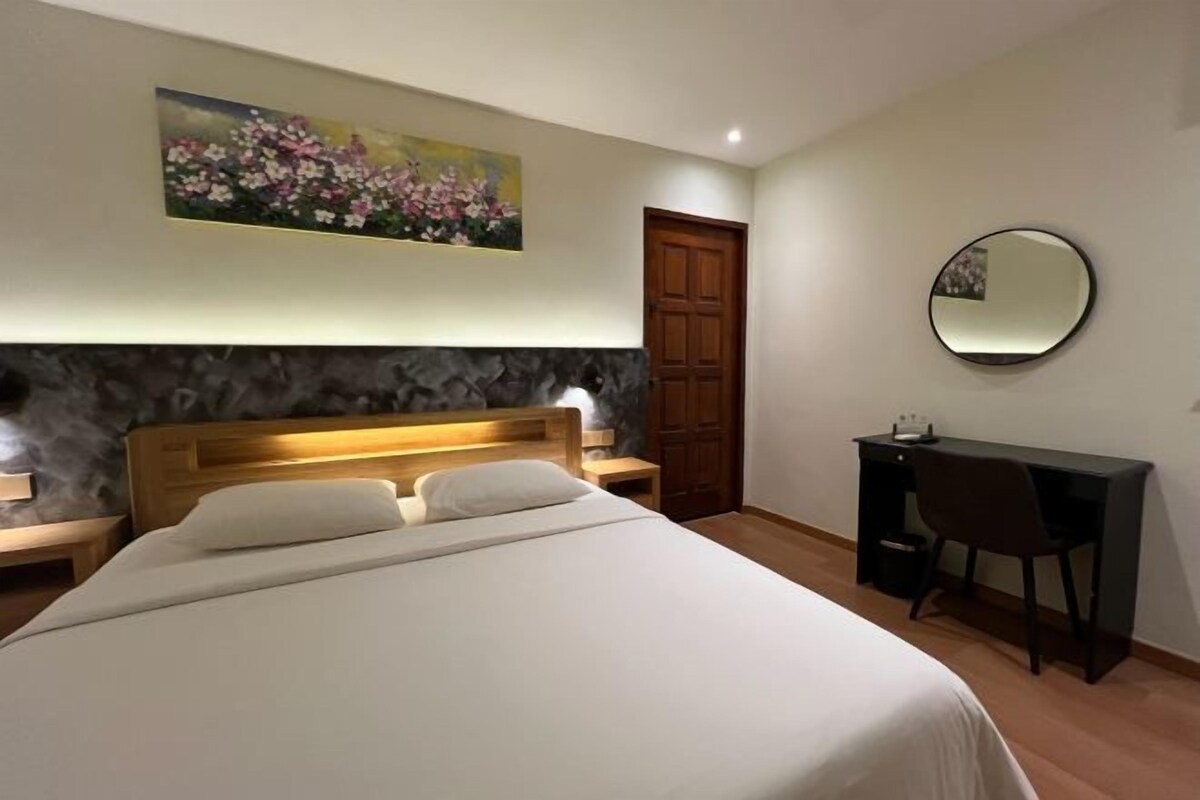 A bedroom with a bed, a desk, a chair, a wooden door, and a painting on the wall.