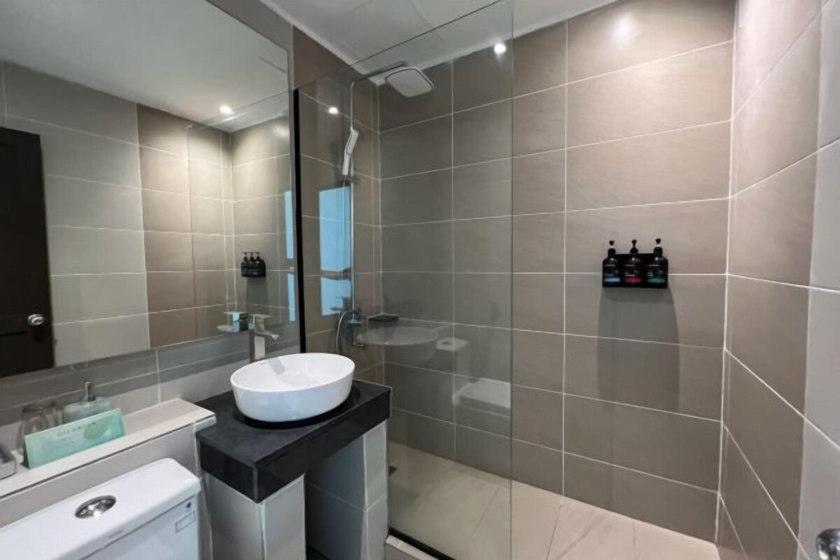 A modern bathroom with a large mirror, a white sink, and a glass-enclosed shower area.
