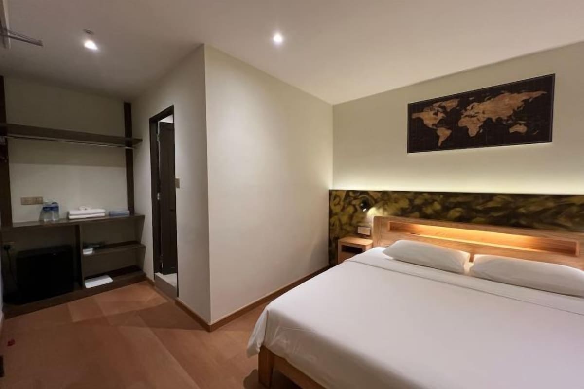 A hotel room with a bed, a desk, and a world map on the wall.