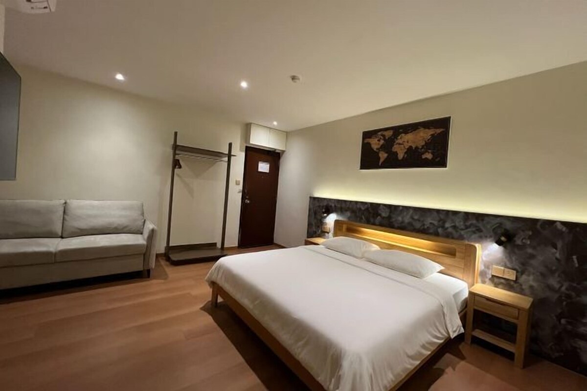 A modern hotel room with a large bed, a sofa, a wardrobe, and a world map on the wall.