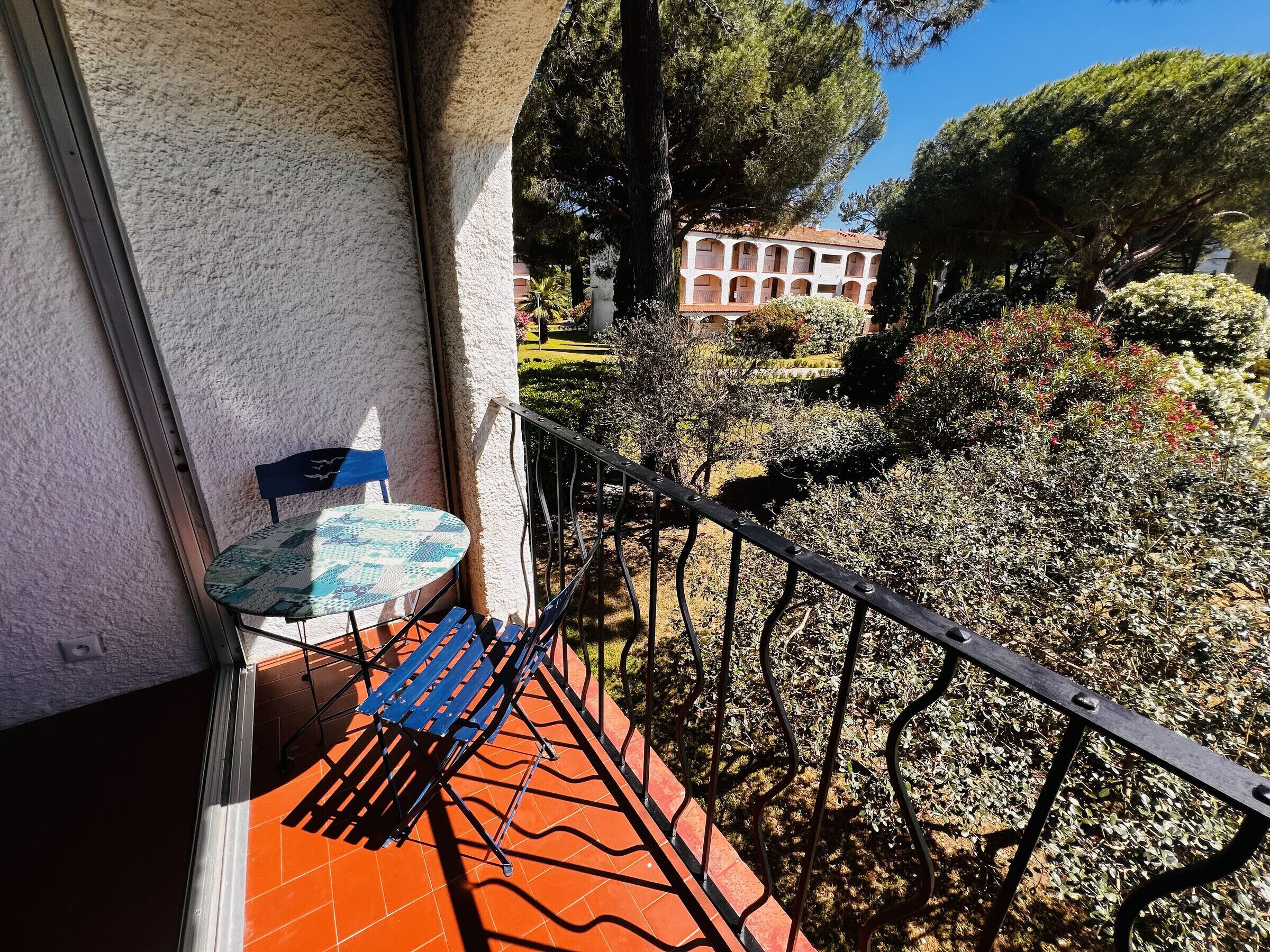 A balcony with a table and chair, a railing, and a view of a building and garden.