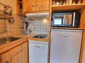 A compact kitchen with a Siemens dishwasher, a Whirlpool refrigerator, a microwave, and a kettle on the countertop.