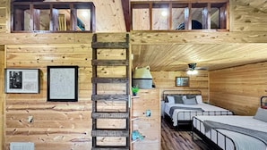Una cabaña con habitación en el altillo, una escalera que lleva a la parte superior y una cama con cabecera.