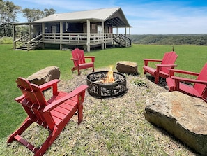 Eine Hütte mit Veranda, Feuerstelle und roten Adirondack-Stühlen.
