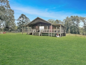 Ein hölzernes Bauernhaus mit Veranda, umgeben von einer grünen Wiese und Bäumen.