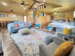 Ein gemütliches Blockhaus-Interieur mit einer Couch, einem Hocker, einem gemusterten Teppich und einem Bett mit Kissen.