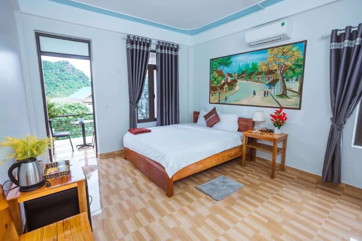 Een slaapkamer met een groot bed, een bureau, een stoel, een potplant en een schilderij aan de muur.