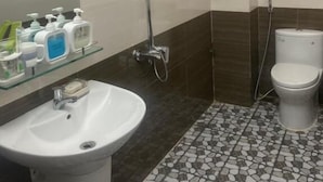 Een badkamer met douche, toilet, wastafel en een glazen plank met toiletartikelen.