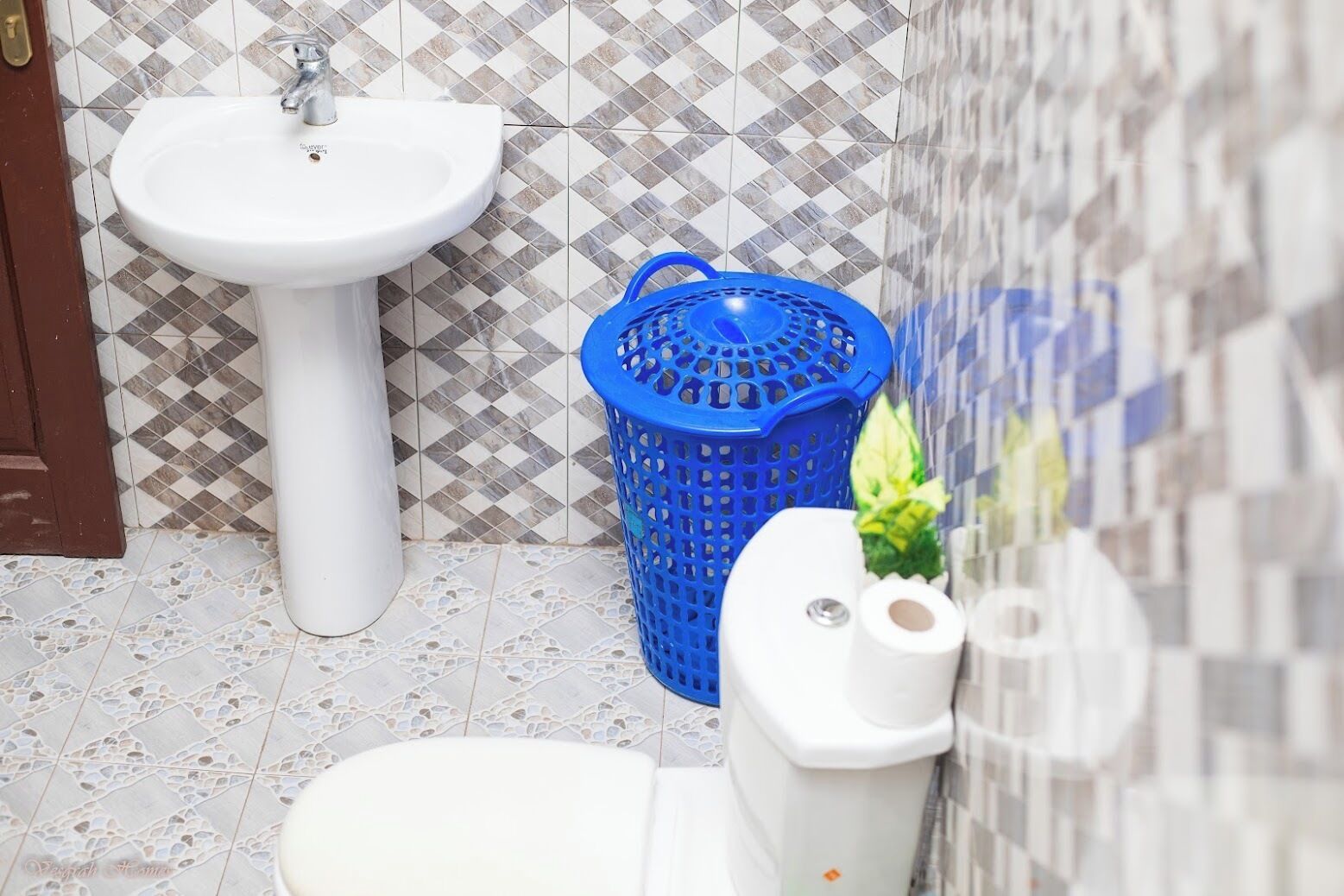 Et badeværelse med en hvid pedikurvask, en blå plastikkurv og et toilet med toiletpapir.