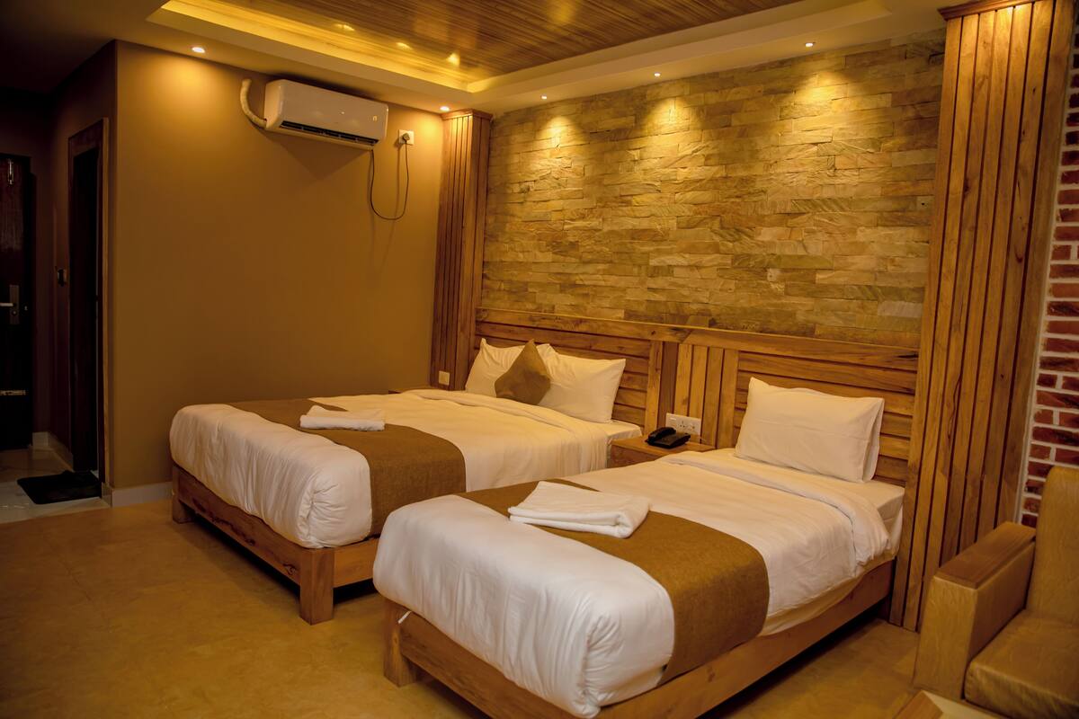 A hotel room with two beds, a brick wall, wooden paneling, and an air conditioning unit.