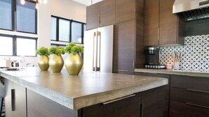 Cozinha moderna com armários escuros, uma ilha grande com bancada e três vasos decorativos com folhagem.