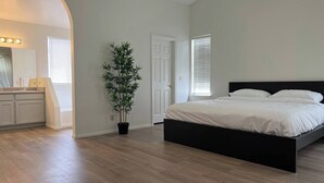 Ein Schlafzimmer mit Bett, einer Topfpflanze und einem Badezimmer mit Waschtisch und Spiegel.
