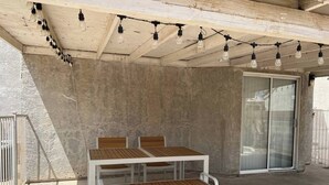 Ein überdachter Patio-Bereich mit einem Holztisch und Bänken, einer Betonwand und einer Schiebetür.