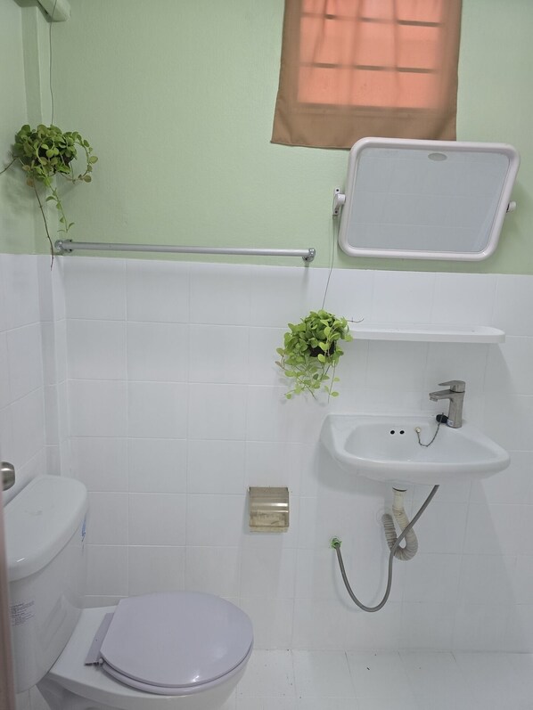 A bathroom with a toilet, sink, and shower. There are plants on the wall and a window above the sink. - Baan Puen Poonsuk (Hua Hin)