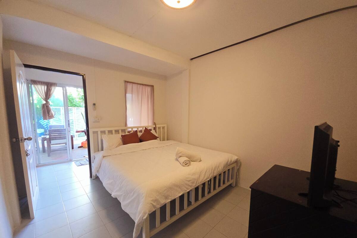 A bedroom with a bed, a television, and a door leading to a balcony.