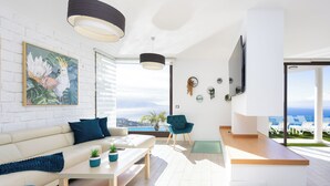 A modern living room with a sofa, coffee table, and chairs, a TV mounted on the wall, and a view of the ocean. - VILLA CANELA, VACATION HOME IN THE NORTH OF TENERIFE (El Sauzal)