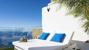 A white bed with blue pillows, a glass table with two wine bottles and glasses, and a view of the sea. - VILLA CANELA, VACATION HOME IN THE NORTH OF TENERIFE (El Sauzal)