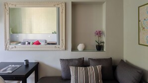 Una sala moderna con un sofá, una mesa de centro, un espejo enmarcado y un estante pequeño con objetos decorativos.