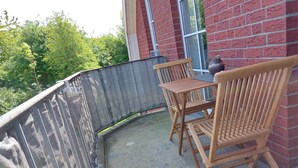 A wooden table and chairs on a balcony with a red brick wall and a window.